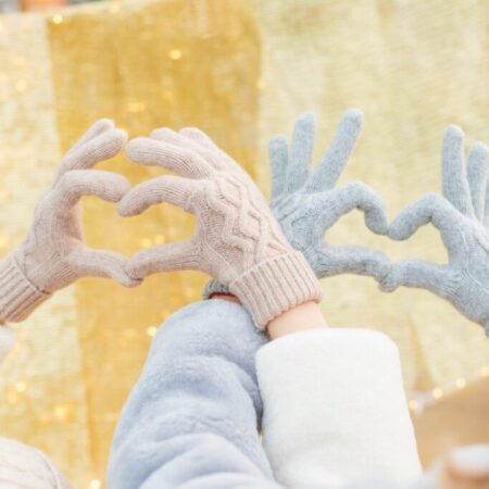 Hands in knitted gloves show peace and heart sign