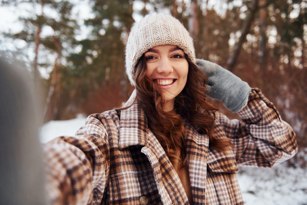 Beautiful woman in warm clothes have a walk in the winter forest