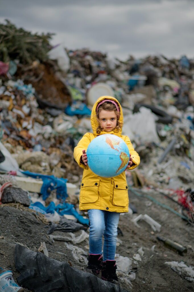 Small child holding globe on landfill, environmental pollution concept